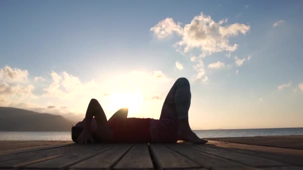 4k - Chica joven hace una pose puente contra la vista del mar de la mañana en cámara lenta — Vídeo de stock