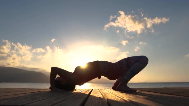 4k-een vrouw maakt een brug pose in de buurt van de zee bij zonsopgang in slow motion — Stockvideo
