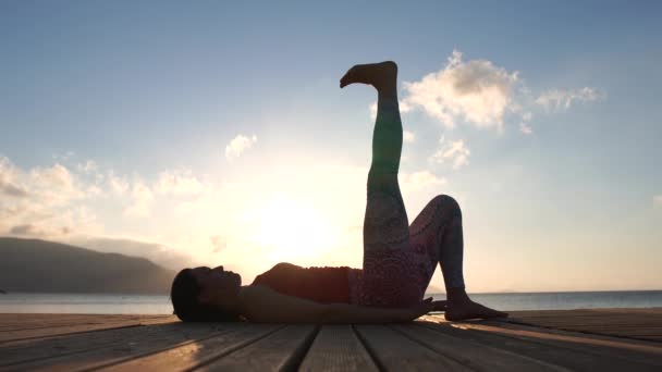 4k-een jong meisje beoefent Pilates op een houten ponton aan de zee in slow motion — Stockvideo