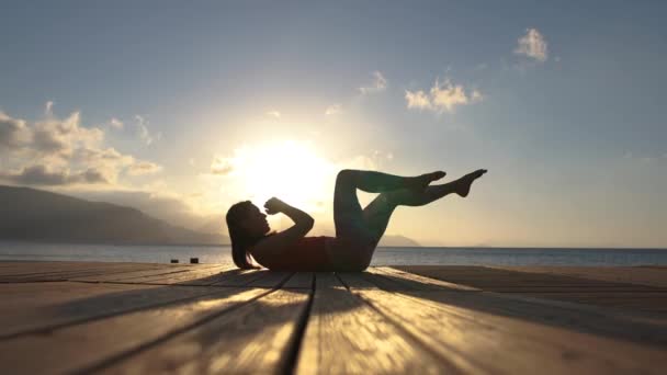 4K-en flicka övningar för ABS vid havet vid soluppgången, slow motion — Stockvideo