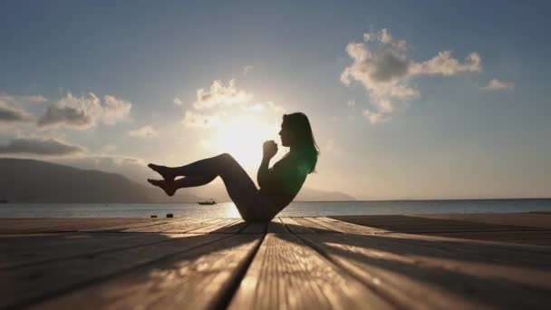 4k-een vrouw doet fitnessoefeningen in de buurt van de zee bij zonsopgang in slow motion — Stockvideo