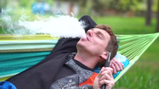 Εύθυμος ξανθός άντρας που βρίσκεται σε μια αιώρα που καπνίζει Χούκα το καλοκαίρι σε αργή κίνηση — Αρχείο Βίντεο