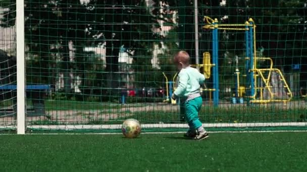 Niño valiente jugando con una pelota en un campo de fútbol en un día soleado en verano en slo-mo — Vídeos de Stock