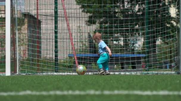 Niño audaz jugando con una pelota en un campo de fútbol en un día soleado en verano en slo-mo — Vídeos de Stock