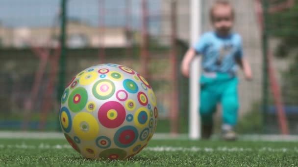 Ευτυχισμένο αγόρι ψυχαγωγεί με μια μπάλα σε ένα γήπεδο ποδοσφαίρου σε μια ηλιόλουστη μέρα το καλοκαίρι σε αργή-mo — Αρχείο Βίντεο