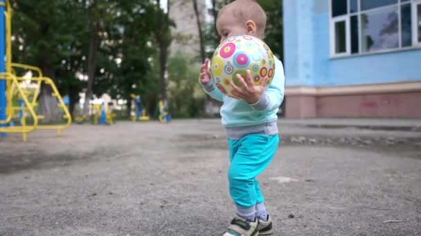 Chico valiente va con una pelota y señala algo en un patio de recreo en slo-mo — Vídeo de stock