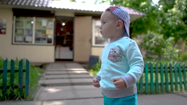 Cheery view of a little blond toddler standing and playing at a wooden fence — Stock Video