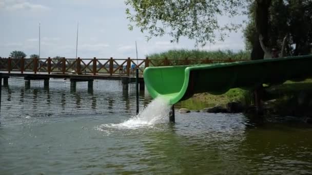 Jonge roodharige kerel glijdt van een waterglijbaan naar een meer in slow motion — Stockvideo