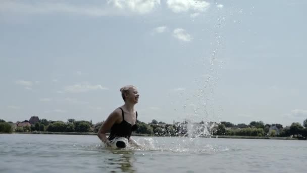 Joven chica rubia feliz salpica agua de pie en el río en cámara lenta — Vídeos de Stock