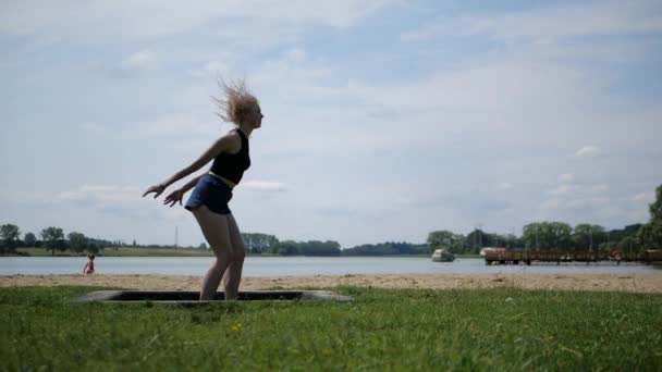 Enérgica chica alegre rubia salta maravillosamente en un trampolín en la naturaleza — Vídeos de Stock