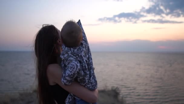 Mother and little kid on her hands at sunset near the sea. — Stock Video