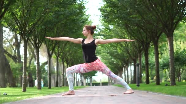 Una joven se para en una pose de yoga en un callejón del parque en cámara lenta — Vídeo de stock