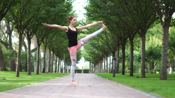 Vacker atletisk flicka utövar yoga i parken i slow motion — Stockvideo