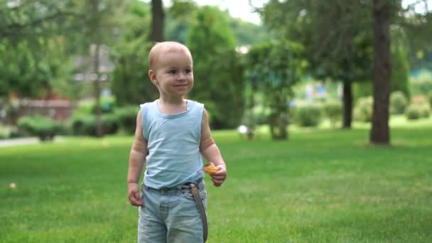 Ένα αγόρι τρέχει χαρούμενα μέσα στο πάρκο με ένα φύλλο στο χέρι του σε αργή κίνηση — Αρχείο Βίντεο