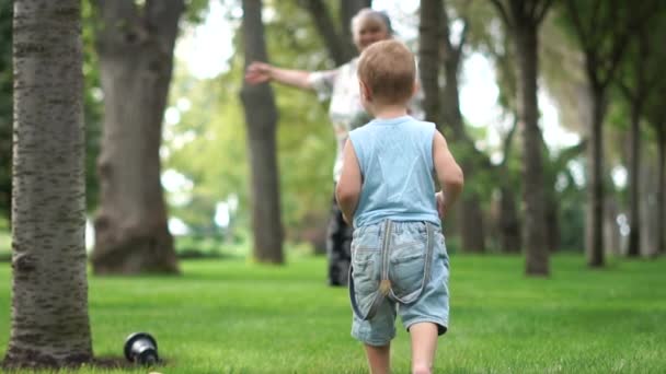 Het kind met zijn oma loopt blootsvoets op het groene gras in slow motion — Stockvideo