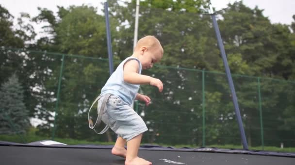 Pequeño chico rubio divertido salta en un trampolín en el parque en cámara lenta — Vídeo de stock