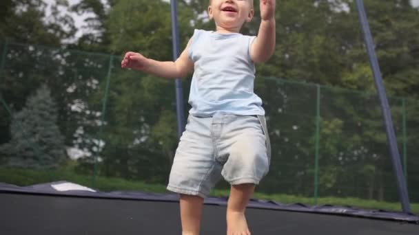Bonito bebê sorridente salta e cai em uma posição sentada em um trampolim . — Vídeo de Stock