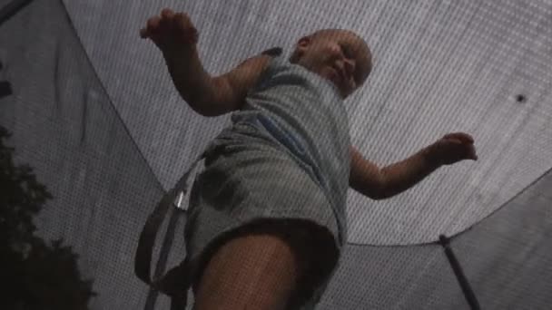 Vista dal basso attraverso la rete su un bambino che salta su un trampolino al rallentatore — Video Stock