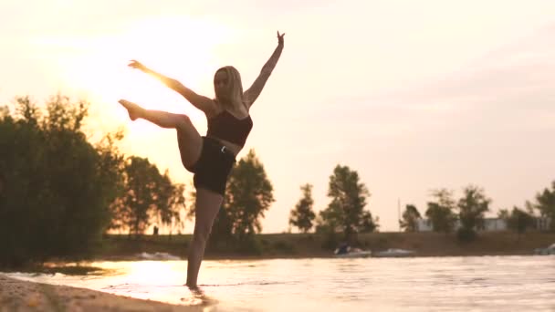 Táncolj napnyugtakor lassítva, szőke fiatal lány táncol a vízben. — Stock videók
