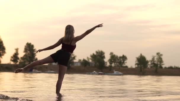 Фаворит танцевальной позы на закате, молодая блондинка танцовщица пытается сделать танцевальную позу и потерпела неудачу в воде. — стоковое видео