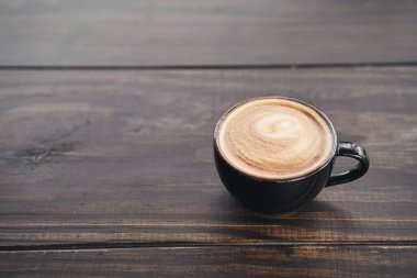 Bir fincan kahve ve ahşap masa üzerinde latte sanatı. Metnin için boşluk.