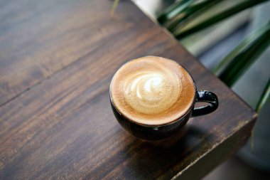 Tahta masanın köşesinde köpüklü sütlü bir fincan kahve. Metnin için boşluk.