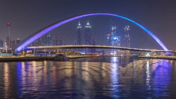 Futurista puente peatonal sobre el canal de agua de Dubai iluminado por la noche timelapse, Emiratos Árabes Unidos . — Vídeo de stock