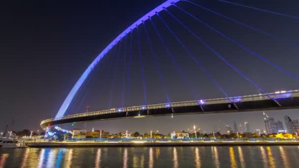 Ponte pedonal futurista sobre o canal de água do Dubai Iluminado no hiperlapso da timelapse da noite, Emirados Árabes Unidos . — Vídeo de Stock