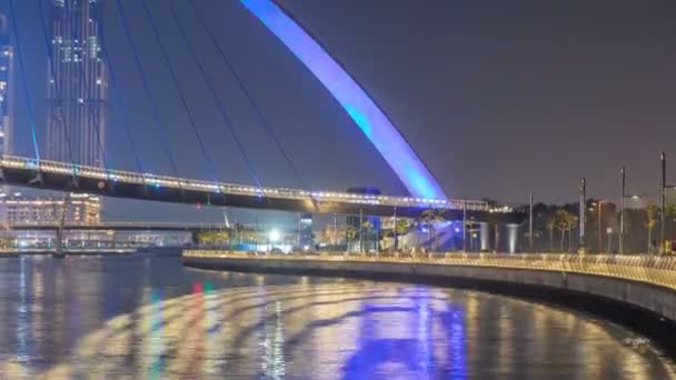 Futurista puente peatonal sobre el canal de agua de Dubai iluminado por la noche timelapse, Emiratos Árabes Unidos . — Vídeos de Stock