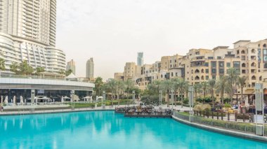 Havuzu ve evlerin en büyük müzikal Çeşmede Dubai günbatımı timelapse yakın. Dubai, Birleşik Arap Emirlikleri. Gökdelenler arka plan üzerinde. Etrafta dolaşan insanlar