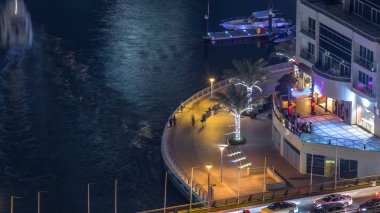 Promenade ve lüks gökdelenler ve yatlar çevresinde gece timelapse, Birleşik Arap Emirlikleri Dubai Marina kanal. Üzerinde yürüme yolu restoranlar ve kafeler ile hava üstten görünüm