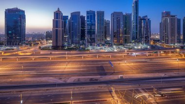 Jumeirah lakes hava görünümünü gün geçiş timelapse Şeyh zayed road ve metro hattı üzerinde trafik ile gecesine ışıklandırılmış gökdelenler ile kuleleri. Dubai Yat Limanı güneş doğmadan önce çatı görünümü