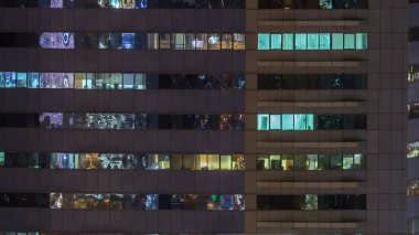 Windows çok katlı binanın içinde aydınlatma ve insanlar timelapse içinde hareketli çelik ve cam. Modern ofis gökdelenler Dubai Hava görünümünü. Vınlamak dışarı