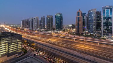 Sheikh zayed road ve metro hattı üzerinde Jumeirah lakes towers gökdelenler gün gece geçiş timelapse trafik için havadan görünümü.