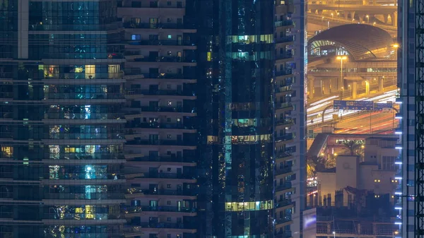 Residential towers with lighting and illumination timelapse. Metro station and promenade on Dubai Marina skyline at night. Traffic near skyscrapers with glowing windows