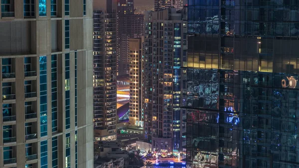 Residential towers with lighting and illumination timelapse. Metro station and promenade on Dubai Marina skyline at night. Traffic near skyscrapers with glowing windows