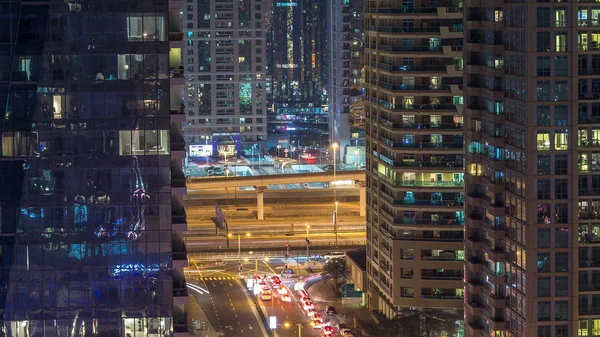 Residential towers with lighting and illumination timelapse. Road and promenade on Dubai Marina and JLT skyline at night. Traffic near skyscrapers with glowing windows