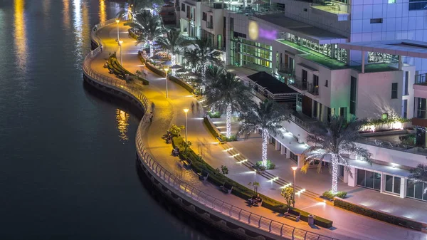 Water canal and promenade on Dubai Marina skyline at night timelapse. Residential towers with lighting and illumination. Floating yachts and boats with traffic near skyscrapers