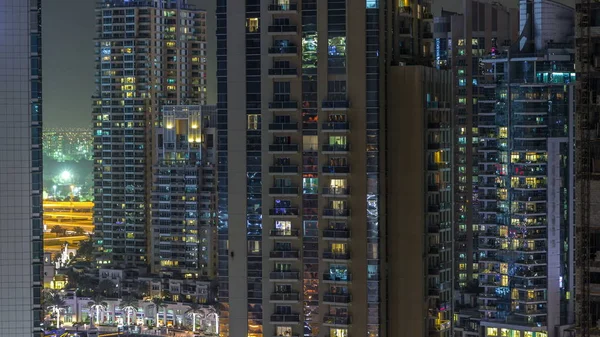 Residential towers with lighting and illumination timelapse. Road and promenade on Dubai Marina and JLT skyline at night. Traffic near skyscrapers with glowing windows