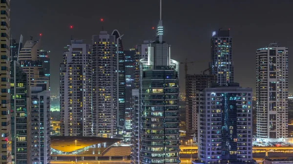 Residential towers with lighting and illumination timelapse. Road and promenade on Dubai Marina and JLT skyline at night. Traffic near skyscrapers with glowing windows
