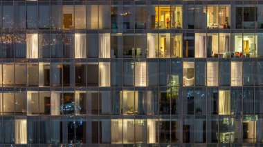 Yanıp sönen ve windows çok katlı binanın cam ve çelik iç aydınlatma ve insanlar timelapse içinde hareketli yanıp sönen. Dubai merkezinde modern konut gökdelenlerin havadan görünümü. Yakınlaştır
