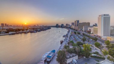 Dubai creek manzara tekneler ve yatlar ile günbatımı timelapse ve trafik yol ve otopark ile modern binalar. Yukarıdan hava üstten görünüm