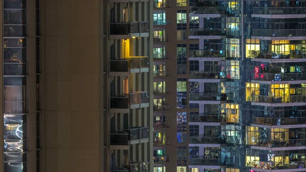 Windows of the multi-storey building of glass and steel lighting inside and moving people within timelapse. Aerial view of modern residential skyscrapers in Dubai marina. Pan down