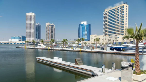 Panoramic timelapse view of business bay and downtown area of Dubai. Modern skyscrapers reflected in water and blue sky. View from promenade on embankment with yachts and boats