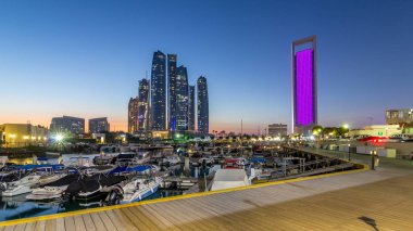 Al Bateen marinası Abu Dabi. Gün batımından sonra tekneler ve arka planda aydınlatmalı modern gökdelenler.