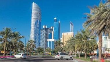 Abu Dabi 'deki sahil şeridi boyunca uzanan Corniche Bulvarı plajı parkında arka planda gökdelenler var. Aile parkından görüntü. Avuçlar yana. Güneşli bir günde mavi gökyüzü