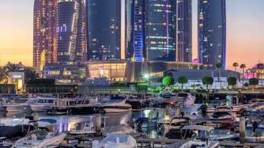 Al Bateen marinası Abu Dabi. Gün batımından sonra tekneler ve arka planda aydınlatmalı modern gökdelenler.