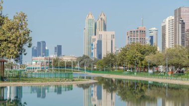 Abu Dabi 'deki sahil şeridi boyunca uzanan Corniche Bulvarı plajı parkında arka planda gökdelenler var. Lake Park 'ın manzarası. Avuçlar yana. Güneşli bir günde mavi gökyüzü