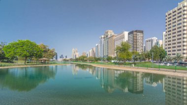 Abu Dabi 'nin sahil şeridi boyunca uzanan Corniche Bulvarı plajı parkında arka planda gökdelenler var. Lake Park 'ın manzarası. Bir tarafta ağaçlar. Güneşli bir günde mavi gökyüzü