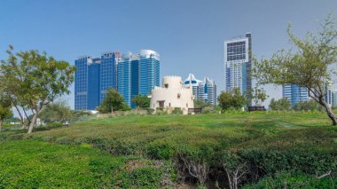Abu Dabi 'nin sahil şeridi boyunca uzanan Corniche Bulvarı plajı parkında arka planda gökdelenler var. Heritage Park 'tan görüntü. Avuçlar yana. Güneşli bir günde mavi gökyüzü